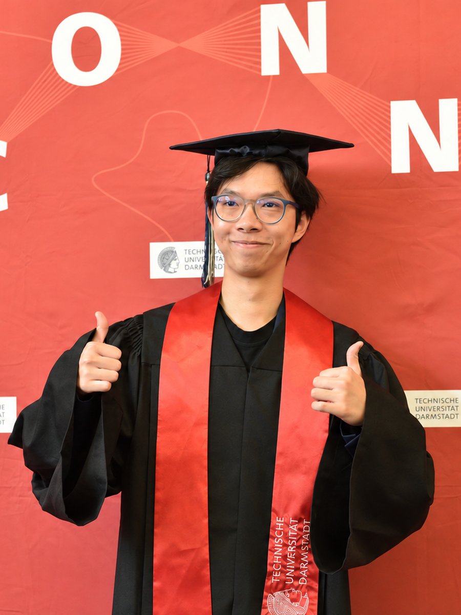 Zhenghua Bao in cap and gown against a TU Darmstadt backdrop